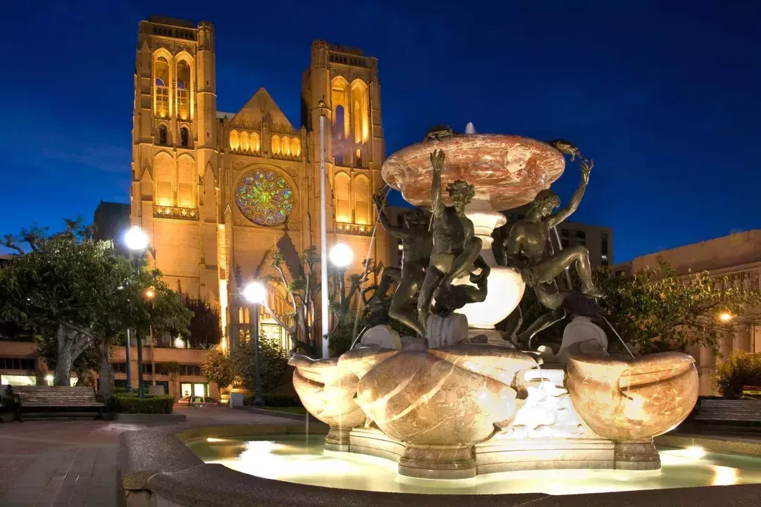 La Catedral Grace de San Francisco aparece fotografiada de noche con una fuente de agua ornamentada en primer plano.